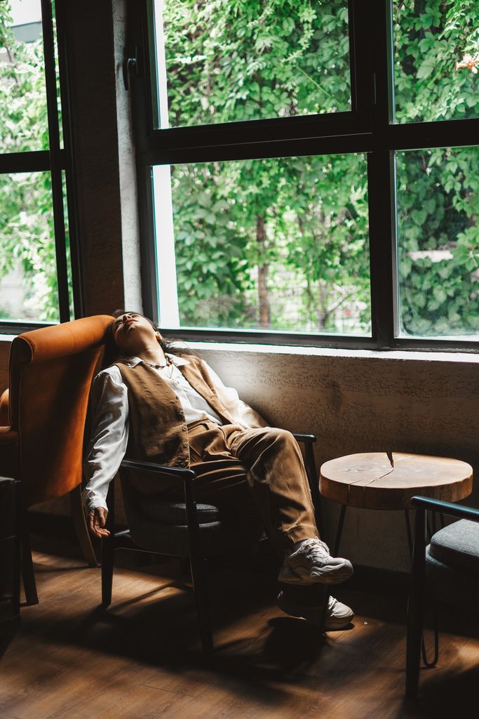 A person rests comfortably by a window in a cozy café, enjoying the serene view of greenery outside.